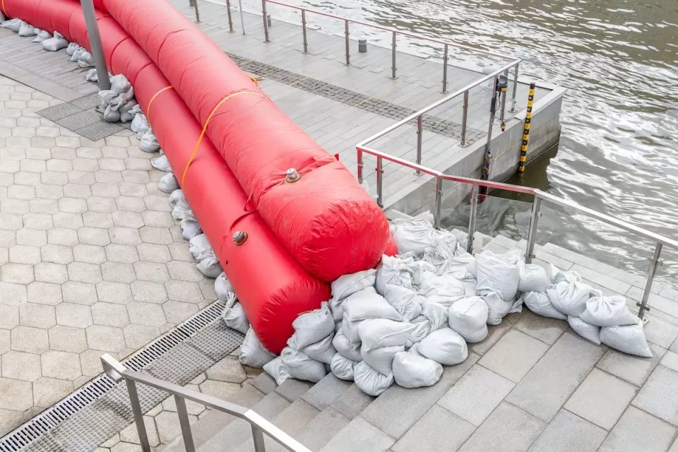 Sandbags and red water-filled cylinders lined up on a concrete pier to prevent flooding.